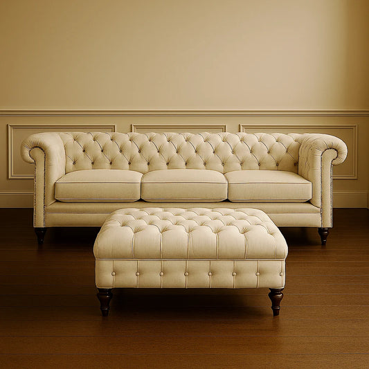 Beige tufted sofa with matching ottoman in a room with wooden flooring and beige walls.
